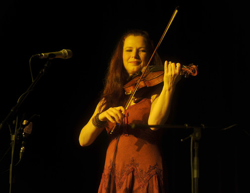 Eine Frau steht auf der Bühne vor dem Mikrofon und spielt auf ihrer Geige.